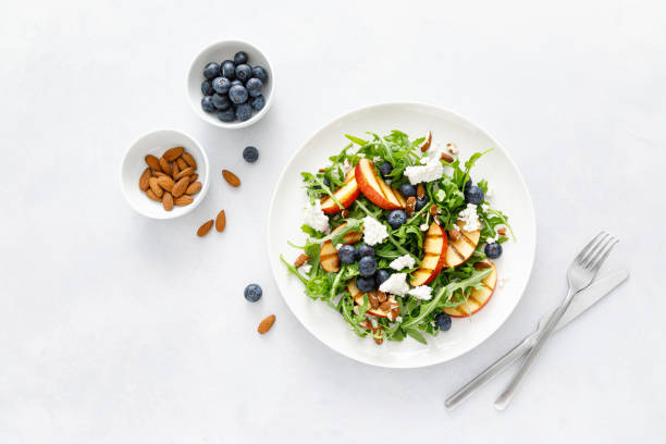 istock Peach, blueberry and arugula fresh fruit salad with cheese and almond nuts, top view 1395140922