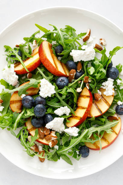 istock Peach, blueberry and arugula fresh fruit salad with cheese and almond nuts, top view 1395140923