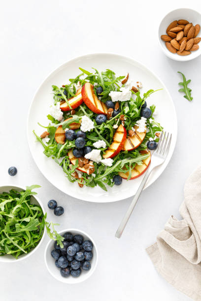 istock Peach, blueberry and arugula fresh fruit salad with cheese and almond nuts, top view 1395140926