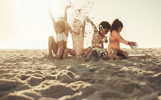 Having fun with beach sand. Adorable little kids laughing cheerfully while throwing beach sand into the air. Group of carefree young friends playing together during summer vacation.