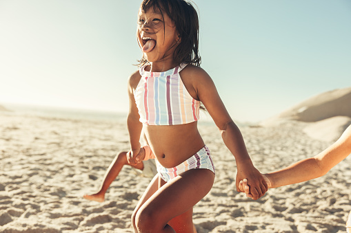 Fun-loving little girl running and having fun with her friends along the beach. Group of happy little children enjoying their summer vacation at a sunny beach.
