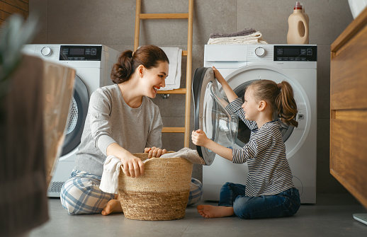 Beautiful young woman and child girl little helper are having fun and smiling while doing laundry at home.