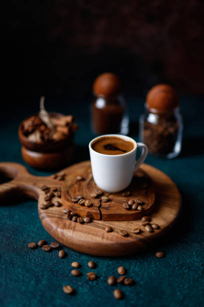 a frothy turkish coffee in a white cup on a round wooden cutting board on a dark turquoise green-blue rough concrete floor - türk kahvesi stok fotoğraflar ve resimler