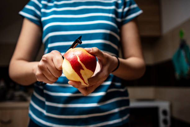 Female hand holding a pear with her fingers from the stem on an isolated light green background, fruit with thin skin juicy pulp with sweet taste of green color