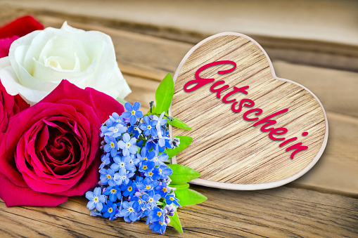 Heart and flowers on wooden background with German gift voucher
