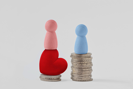 Pink pawns with heart and blue pawn on piles of coins - Concept of woman power and gender pay gap