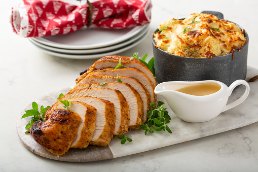 Roasted turkey breast sliced on a plate for holiday dinner with gravy and cauliflower casserole