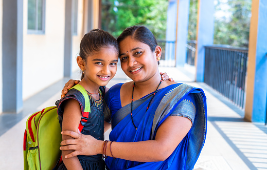 happy smiling Mother embracing her daughter before going to classroom at school corridor by looking at camera - concept of back to school, relationship and parental love.