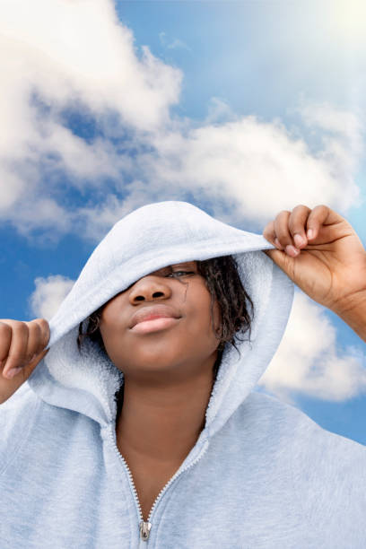 young african american teenage girl playing with her hoodie, fifteen years old, braided hair, sunny day, blue sky, white clouds - 13 14 years teenager school education imagens e fotografias de stock