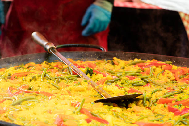 Cooking seafood paella in a large pan at outdoor kitchen.