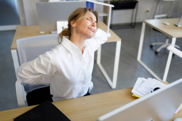 istock Business woman holding her lower back while working at a computer in the office. Problems with the spine due to sedentary work 1395161872