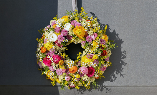 Flower wreath hanging on a house wooden door. Fresh wild flowers and herbs, home decoration, front view. Spring sunny day. Women or mothers day celebration