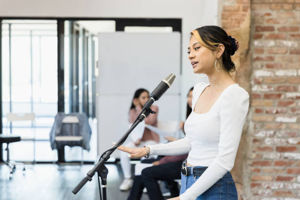 istock Young woman stands at microphone to perform monologue 1395164234