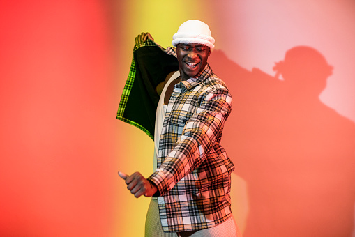 Man opening his jacket while dancing looking at the camera in front of a multi coloured studio background. He is in the North East of England.