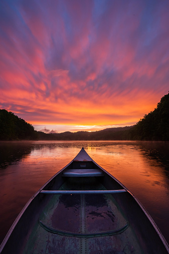 A colorful sunset fills the sky and reflects on the surface of a mountain lake as seen from the seat of this old aluminum canoe