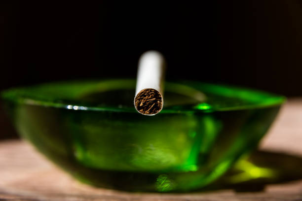 istock cigarette front view leaning on a green glass ashtray, black background 1395166808