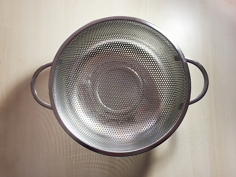 Silver colored stainless steel colander on the wood table