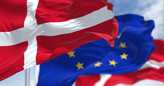 Detail of the national flag of Denmark waving in the wind with blurred european union flag in the background on a clear day
