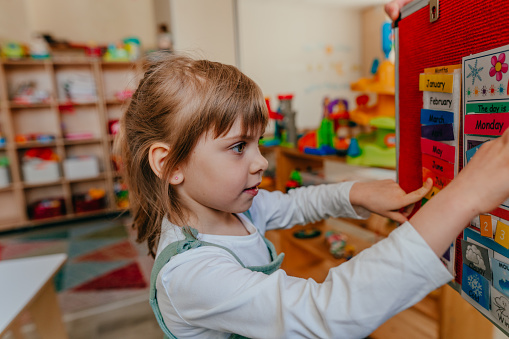 Little girl learning days of week at kindergarten. Didactic materials on the velcro board using for preschool education. Selective focus.