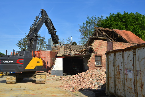 Wilsele, Vlaams-Brabant, Belgium - May 03, 2022:  Volvo EC250EL excavator dismantling a car repair garage building in brick. First floor being grabbed by bucket bulldozer