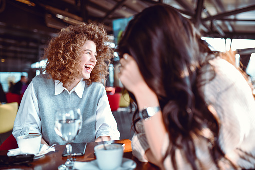 Cute Female With Curly Hair Smiling After Hearing A Joke From Her Friend