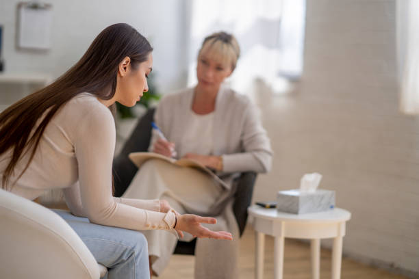 Distraught Woman in Therapy A young woman of Ukrainian decent, sits with a therapist as she talks through her struggles and depression. She is dressed casually and appears distraught as the leans forward and rests her elbows on her knees. The therapist is dressed professionally and has a notepad out on her lap as she takes notes and looks at the woman sympathetically. Inpatient addiction Treatment stock pictures, royalty-free photos & images