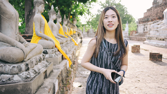 Asia Female tourist smile happy taking pictures with smart phone walking tour visiting Ayutthaya Province, Wat Yai Chai Mongkhon