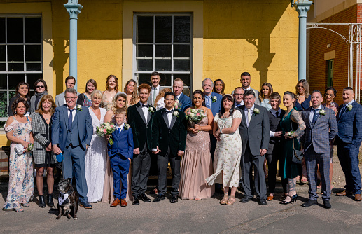 A full length wide angle view of a full wedding party stood outdoors together after the wedding of two men in County Durham in the North East of England.