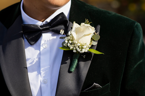 A close-up of an unrecognizable man wearing his green velvet wedding blazer with his boutonniere attached to his green velvet wedding blazer in anticipation of the big day.