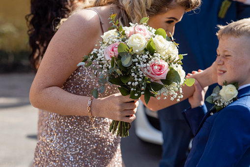 A tender moment between family members at a wedding in Durham in the North East of England. She is carrying a bouquet and dressed for a wedding and the young boy is recoiling as his face is affectionately touched
