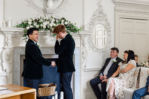 A mid-length front view of two grooms on their wedding day. one of the men with red hair is getting emotional as he makes his vows to his husband.