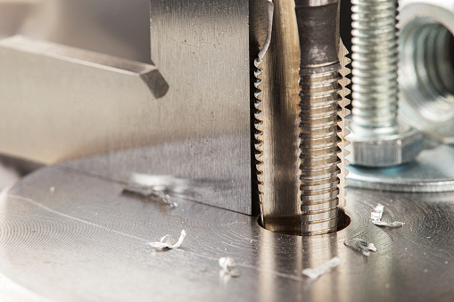 Thread tap drill steel billet with drill bit on background. Working cutter.