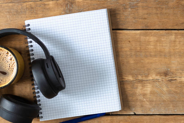 Blank notebook with pen, headphones and coffee cup on wooden table. Writing notes, planning concept