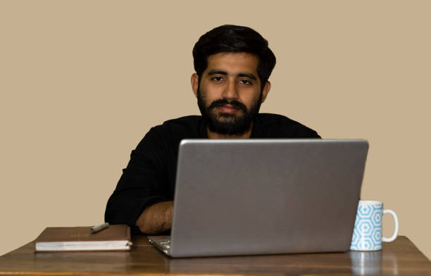 istock A young indian man looking at the camera while working on laptop. 1395187761