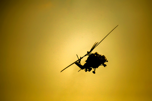 Silhouette of a military helicopter flying during sunset.