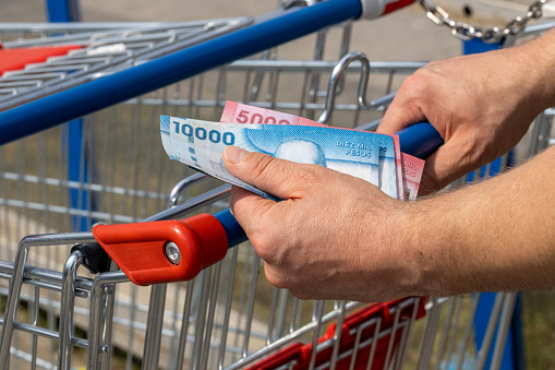 Shopping cart in a supermarket and Chile money held in hand, Concept of inflation, Rising costs of living, Home budget