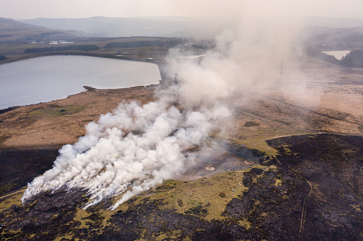 Aerial view of a huge wildfire on higher level moorland next to a reservoir (Llangynidr Moors, Wales)