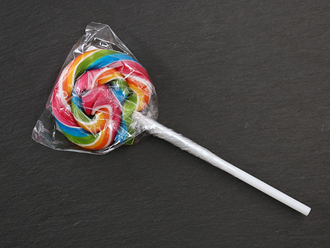 single colorful lollipop wrapped in plastic packaging on black background, top view.