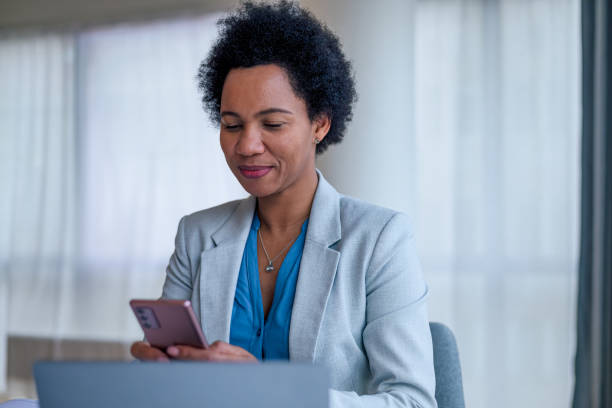 istock Smiling businesswoman messaging on smart phone while working on laptop at office 1395195111