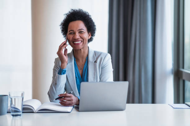 istock Smiling businessman talking on smart phone while using laptop at office desk 1395195150