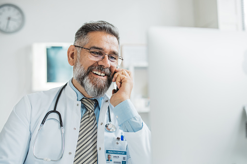 Doctor talking on smart phone while explaining medical treatment to patient.