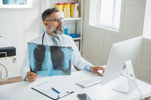 Doctor analyzing x ray image of lungs. He is sitting at office and working on computer.