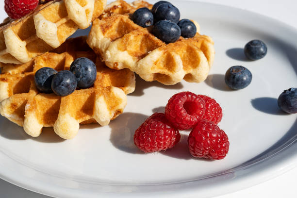 Homemade waffles with raspberries and blueberries on a plate, dessert for breakfast, close-up.