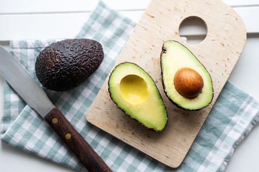 Fresh avocado halves on cutting board on white background, healthy vegan food.