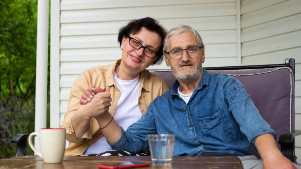 retrato de una pareja de ancianos sonriendo sentada en el sofá de la terraza de la casa al aire libre. feliz y agradable familia anciana mirando a la cámara, tomados de la mano. encantador hombre y mujer caucásico maduro y retirado que descansa en la te - armenian ethnicity fotografías e imágenes de stock