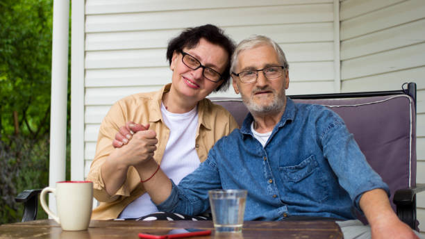 portrait of senior couple smiling sitting on sofa on home terrace outdoor.happy nice elderly family looking at camera,holding hand.lovely caucasian mature and retired man and woman resting on veranda - armenian ethnicity imagens e fotografias de stock