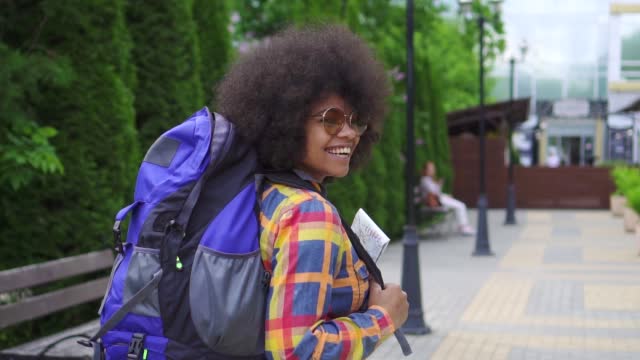 black woman tourist with an afro hairstyle and backpack behind rear view slow mo urban landscape