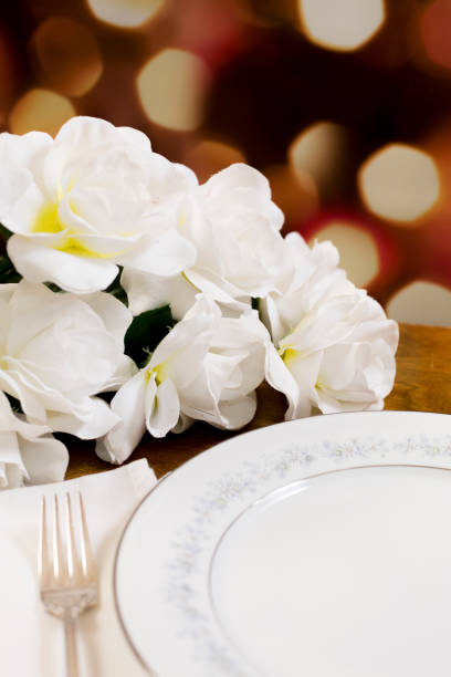 istock Place setting on table with bouquet of white roses. 1395200820