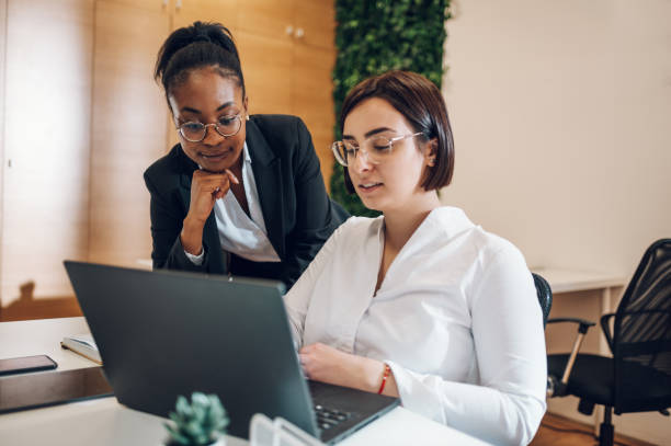 istock Two diverse female designers smiling while working together on a laptop during a meeting in a modern office. Businesswomen sharing ideas. 1395201074