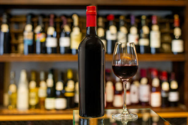 Bottle and glass of red wine in a store with a variety of bottles in the background out of focus stock photo